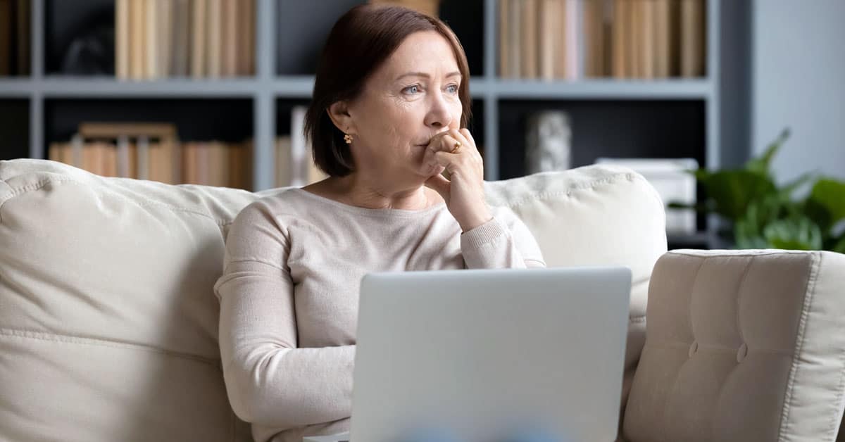 Woman sitting on couch with laptop with a look of concern